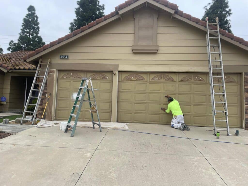 Expert painter applying fresh paint to garage door at residential property.